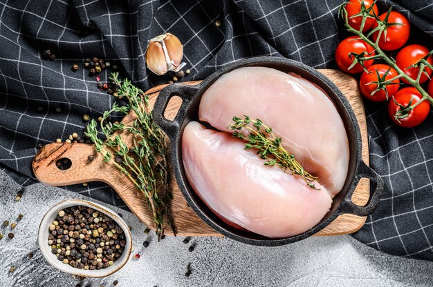 Rohes Hähnchenbrustfilet in einer Pfanne mit Kräutern und Gewürzen. Weißer Hintergrund. Draufsicht