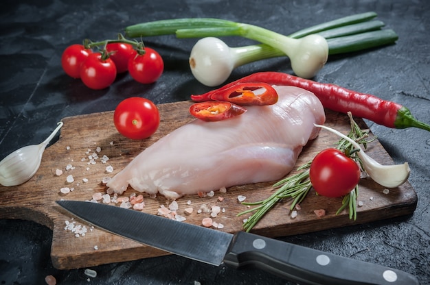 Rohes Hähnchenfilet auf Schneidebrett, Chili und Tomaten