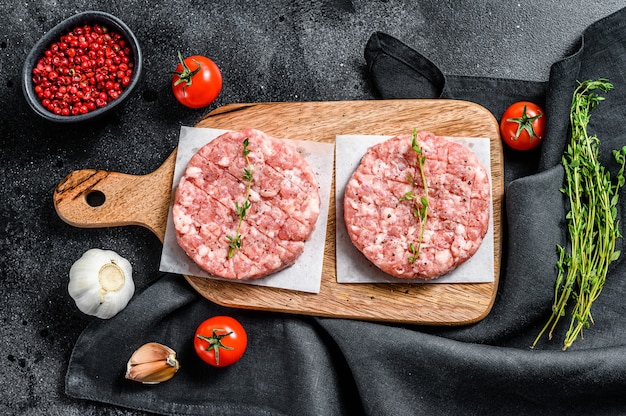 Rohes Hühnchenpastetchen, Hackfleischkoteletts auf einem Schneidebrett. Bio-Hackfleisch. Schwarzer Hintergrund. Draufsicht