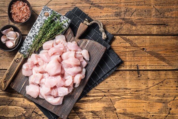 Rohes Hühnerfilet in Würfel geschnitten, ungekochtes geschnittenes Geflügelfleisch, auf Holzbrett. Hölzerner Hintergrund. Ansicht von oben. Platz kopieren.