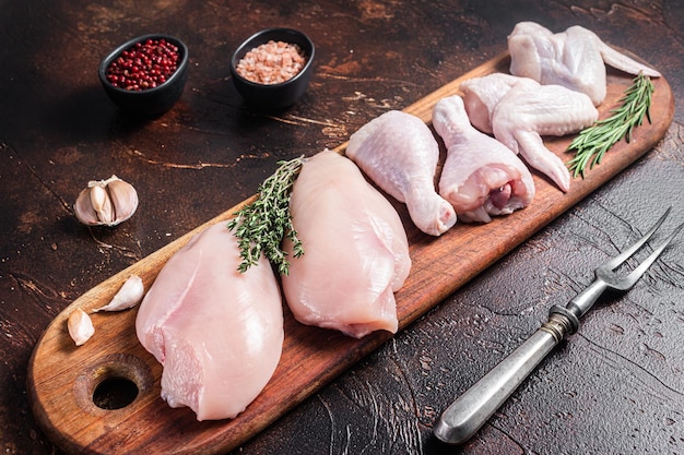 Rohes Hühnerfleischsortiment aus Teilen Drumstick Brustfilet Flügel Oberschenkel mit Gewürzen Dunkler Hintergrund Ansicht von oben