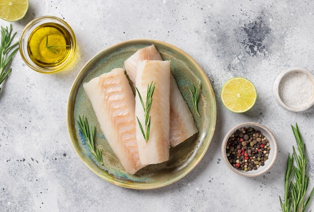 Rohes Kabeljaufilet auf Keramikplatte mit aromatischen Kräutern