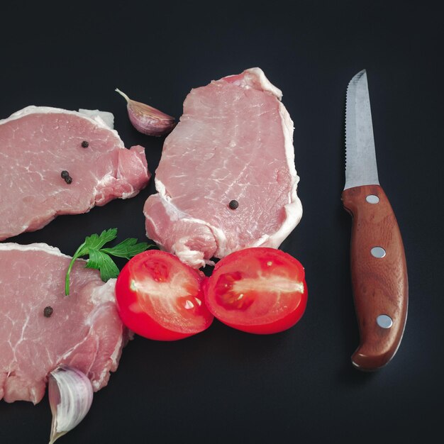 Rohes Kalbsfleischfilet auf Küchenschneidebrett mit Zutaten zum Kochen auf dunklem Hintergrund
