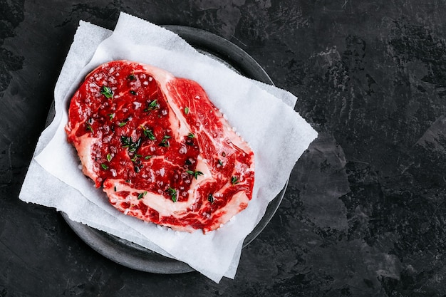 Rohes Kalbsrindsteak auf einem Papier mit Salz und Thymian auf dunklem Steinbetongrund Draufsicht mit Kopierraum