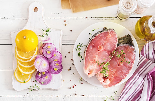 Rohes Karpfensteak mit Zitrone und Thymian auf weißer Holzoberfläche. Fisch zum Braten in Pergamentpapier vorbereiten. Diätmenü. Draufsicht. Flach liegen