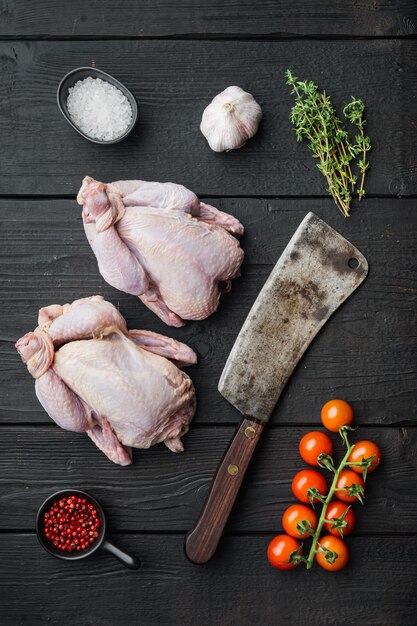 Rohes kleines junges Huhn mit Kräutergewürzzutaten, auf schwarzem Holztisch, Draufsicht