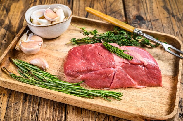 Rohes Lammfleischsteak in einem Holztablett mit Kräutern