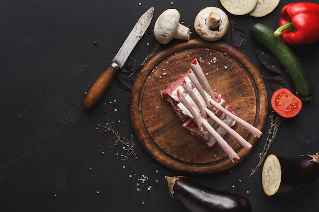 Rohes Lammkarree. Frisches Fleisch, Rosmarin und Kräuter, Pfeffer, Tomaten auf Holzbrett auf dem Tisch. Bio-Zutaten für Restaurantmahlzeiten, Draufsicht, Kopierraum