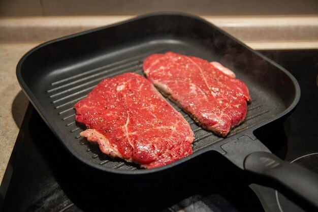 Rohes Minutensteak vom marmorierten Rindfleisch in einer Grillpfanne auf einer elektrischen Kochfläche