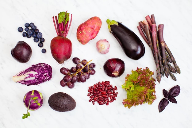 Rohes purpurrotes Gemüse und Früchte über weißem Marmorhintergrund. Ansicht von oben, flach liegend.