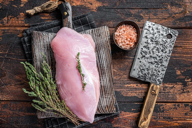 Rohes Putenbrustfilet auf einem hölzernen Metzgerbrett mit Fleischerbeil. Dunkler Holztisch. Draufsicht.