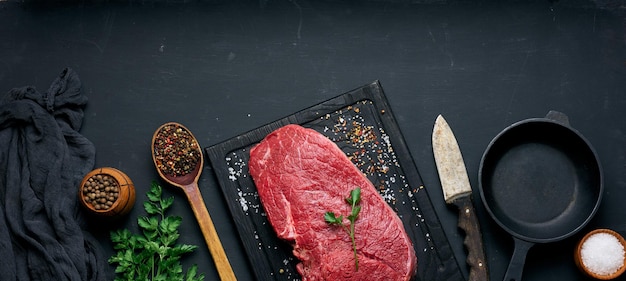 Rohes Rinderfilet liegt auf einem Holzschneidebrett und Gewürzen zum Kochen auf einer schwarzen Tischplatte