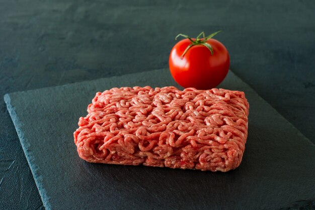 Rohes Rinderhackfleisch auf einer Schiefertafel mit Tomate.