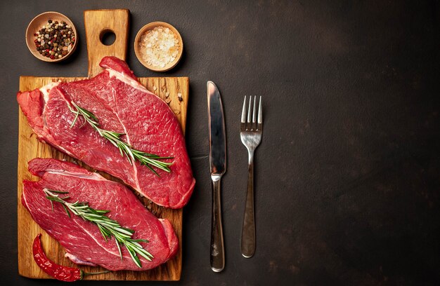 rohes Rindersteak auf einem Schneidebrett mit Gewürzen auf einem Steinhintergrund mit Kopierraum für Ihren Text