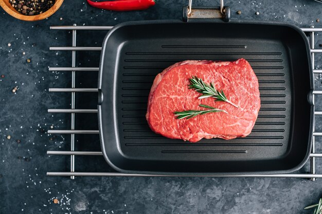 Rohes Rindersteak auf schwarzer Grillpfanne mit Rosmarin