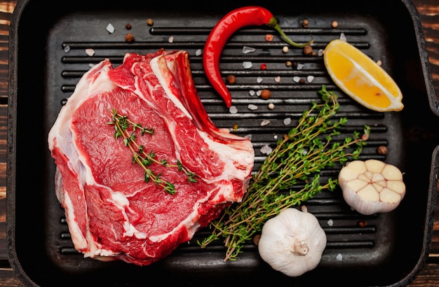 rohes Rindersteak in einer Grillpfanne mit Gewürzen auf einem Holzhintergrund