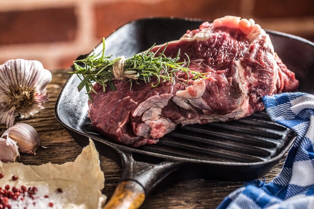 Rohes Rindersteak in Grillpfanne mit Salzpfefferknoblauch und Kräutern auf Holztisch.