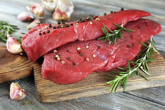 Rohes Rindersteak mit Rosmarin und Knoblauch auf Schneidebrett auf Holzhintergrund