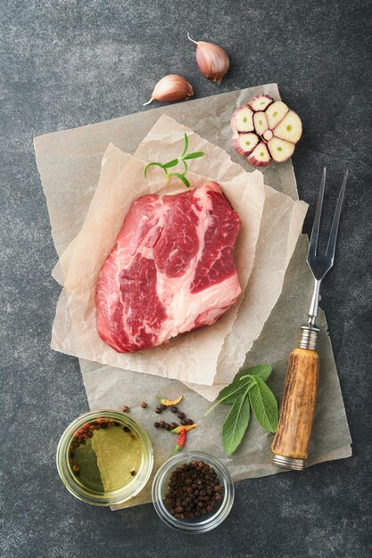 Rohes Rindersteak Rohes frisches Chuck-Roll-Steak mit Rosmarinsalz und Pfeffer auf Schneidebrett auf dunklem Betongrund Rohes Rindersteak und Gewürze zum Kochen