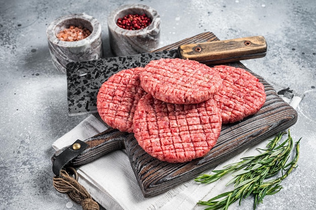 Rohes Rindfleisch Burger Patties auf Metzger Holzbrett mit Fleischerbeil Grauer Hintergrund Ansicht von oben