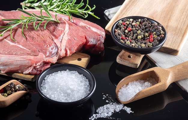 Rohes Rindfleisch geschnitten auf einem Schneidebrett mit Holzlöffel mit Salz und Pfeffer Schwarzer Hintergrund Ansicht von oben