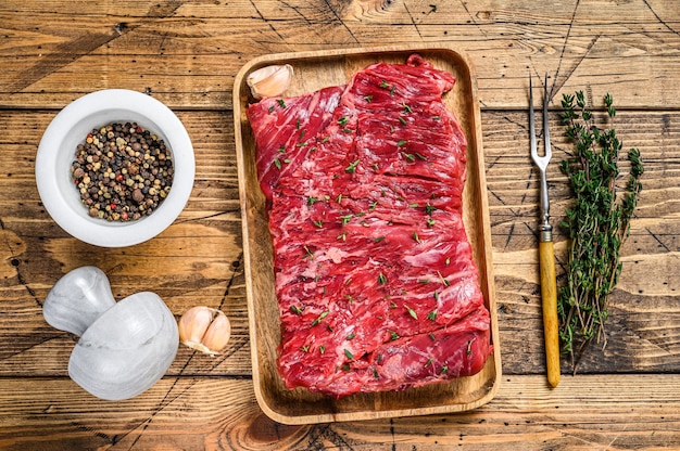 Rohes Rindfleisch rund geschnittenes Fleisch auf einem Holztablett mit Kräutern. hölzerner Hintergrund. Ansicht von oben.