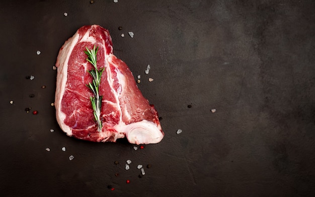 Rohes Rindfleisch-T-Bone-Steak mit Gewürzen auf dem Hintergrundstein. mit Kopierplatz für Ihren Text.