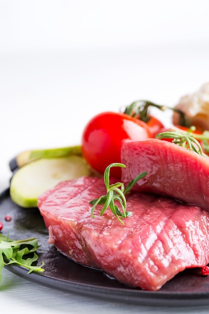 Rohes Rindfleischsteak mit Frischgemüse in einer Wanne auf einem Marmorhintergrund