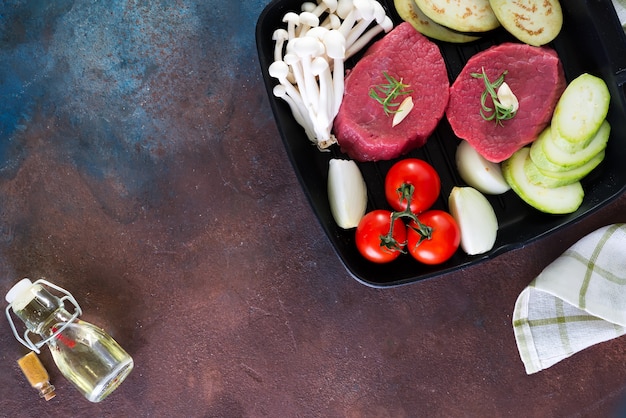 Rohes Rindfleischsteak mit Knochen mit Frischgemüse in einem Draufsicht copyspace der Wanne