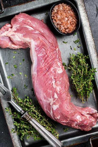 Rohes Schweinefilet in Stahlplatte mit Kräutern, schwarzer Hintergrund, Top-View