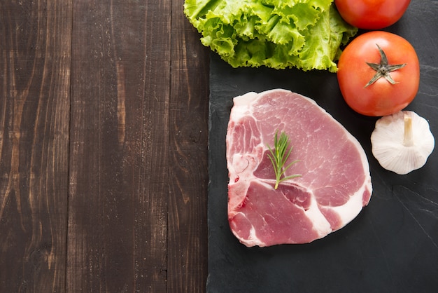 Rohes Schweinefleisch der Draufsicht auf Tafel und Gemüse auf Holztisch