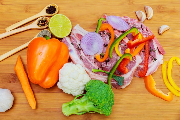 Rohes Schweinefleisch in der Marinade, auf einem Schneidebrett mit Tomatenniederlassung, Messer für Fleisch und Gewürzgrenze, Draufsicht des hölzernen Hintergrundes des Platztextes