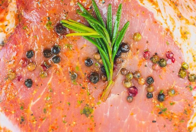 Rohes Schweinefleisch mit Gewürzen und grünem Rosmarinkraut. Texturhintergrund des roten Fleisches, roher Schinken. Makrofoto. Fett Frisches saftiges Steak.