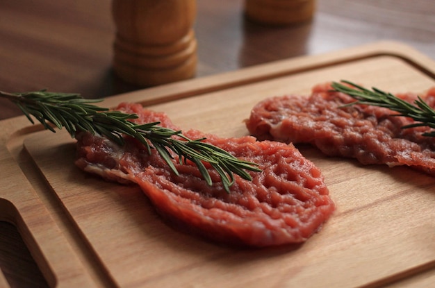 Rohes Schweinekotelett mit Gewürzen und einem Rosmarinzweig auf einem Holzbrett