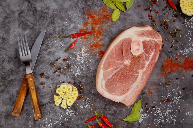 Rohes Schweinekotelett mit Gewürzen und Hackmesser auf dunklem Hintergrund. Ansicht von oben.