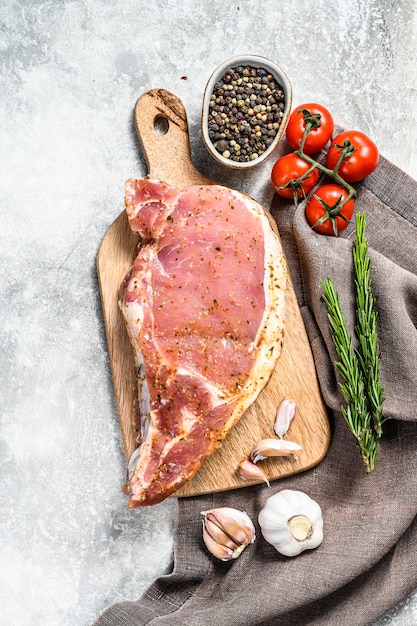 Rohes Schweinekotelettsteak auf einem hölzernen Schneidebrett. Grauer Hintergrund. Draufsicht