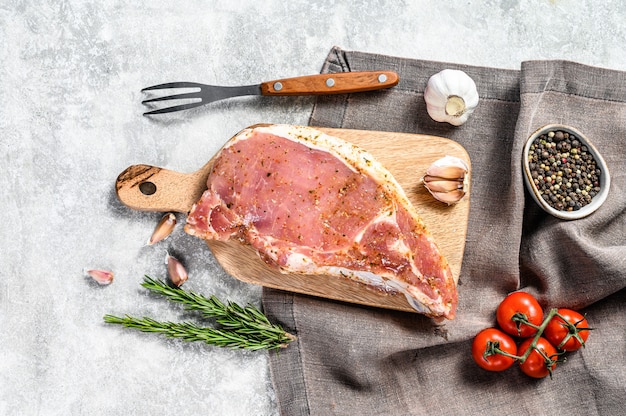 Rohes Schweinekotelettsteak auf einem hölzernen Schneidebrett. Grauer Hintergrund. Draufsicht