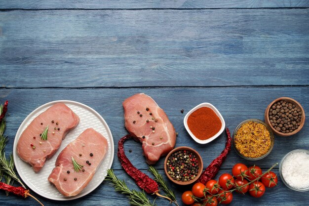 Rohes Schweinesteak auf einem Teller, Fleisch und Zutaten zum Kochen, Gewürzkräuter und Gemüse auf hellem Hintergrund. Ansicht von oben