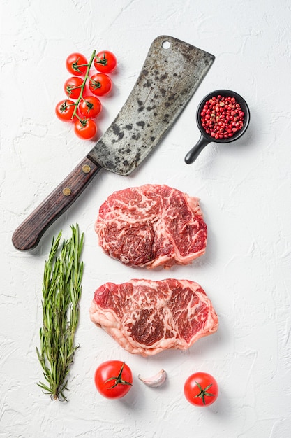 Rohes Spitzensteak, Bio-Fleisch mit Gewürzen, Rosmarin und Metzgerbeil. Weißer strukturierter Hintergrund. Ansicht von oben.