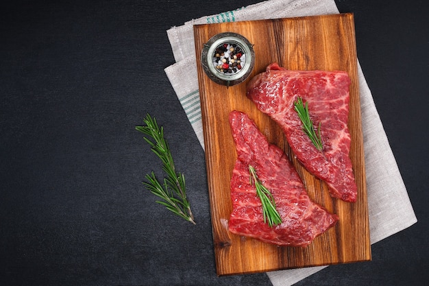 Rohes Steak auf Schneidebrett mit Rosmarin und Gewürzen