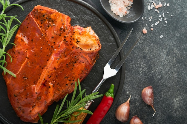 Rohes Steak tbone oder Porterhouse Steak tbone oder Porterhouse in Sauce mit Gewürzen, Salz und Rosmarin auf einer schwarzen Keramikplatte auf Betongrund Draufsicht Platz für Text