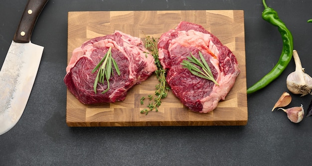 Rohes Stück Beef Ribeye mit Rosmarin, Thymian auf einem schwarzen Tisch, Draufsicht