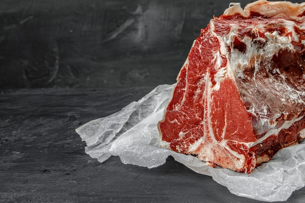 Rohes T-Bone-Steak, das auf dunklem Steintisch kocht.