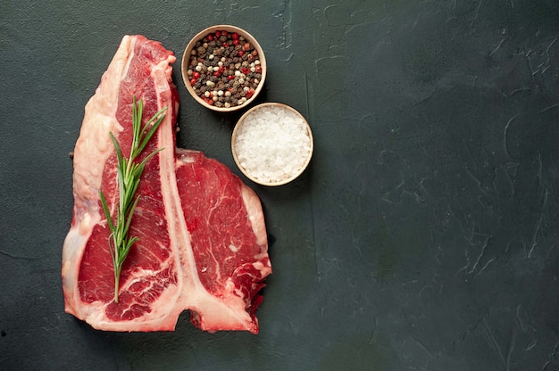 Rohes T-Bone-Steak mit frischen Kräutern auf einem Beton- oder Schieferhintergrund, Draufsicht, Platz für Text