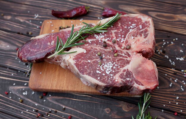 rohes T-Bone-Steak mit Rosmarin, Pfeffer und Olivenöl auf einem zum Kochen vorbereiteten Schneidebrett