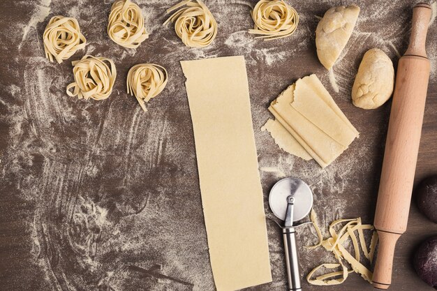 Rohes Tagliatelle-Nest und Teigscheiben mit Radschneider auf dem Küchentisch. Zubereitung hausgemachter italienischer Pasta, Draufsicht, Kopierraum