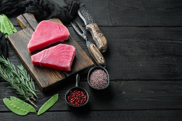 Rohes Thunfischsteak, frisches rotes Thunfischfilet mit Zutaten, grüne Erbsen, Sesam und Gewürze, auf Holzbrett, auf schwarzem Holztisch