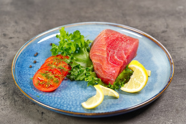 Rohes Thunfischsteak mit Salat und Zitrone auf blauem Teller