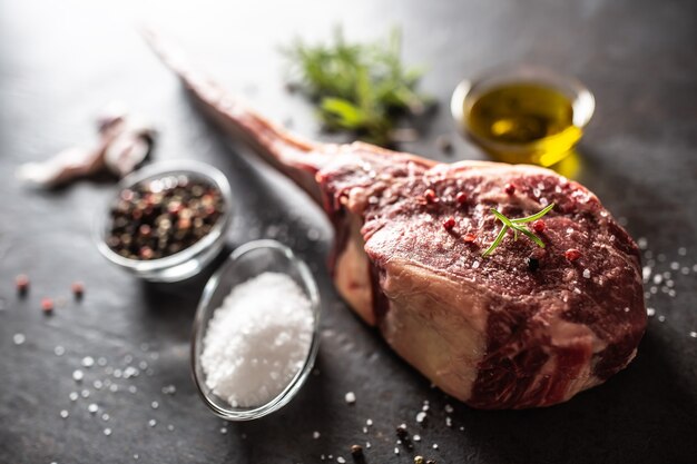 Rohes Tomahawk-Steak mit Salz würzt Knoblauch und Kräuter auf einem alten rustikalen Brett.