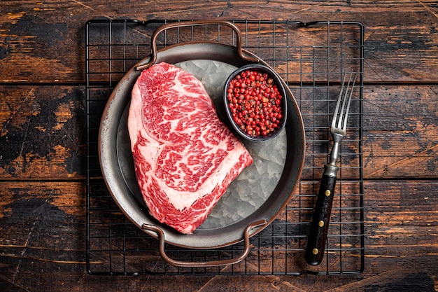 Rohes Wagyu-Rib-Eye-Rindfleischsteak in Stahlschale Holzhintergrund Ansicht von oben